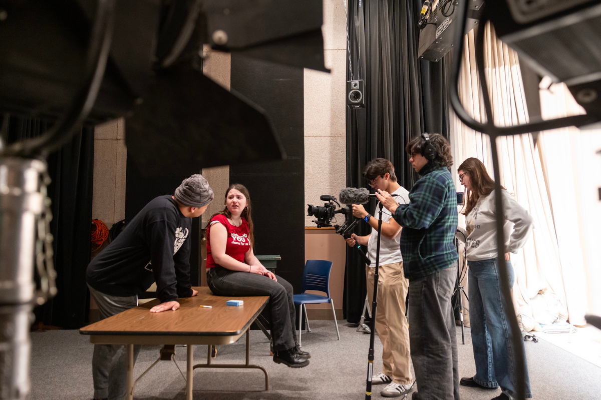Students on left side of image act on set while students on right side of image film them