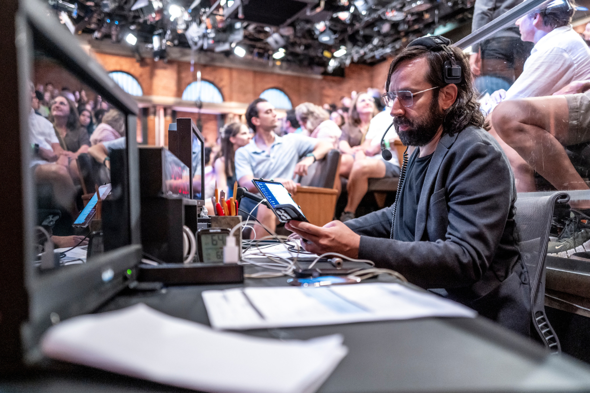 Eric Leiderman situated at a desk looking at equipment in front of a studio audience