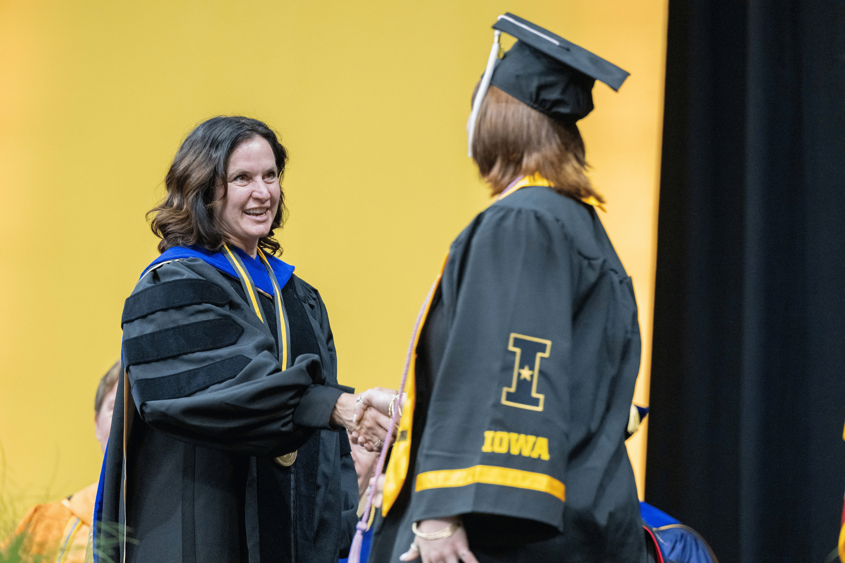 CLAS Dean Sara Sanders shakes hands with a graduate on state at Commencement