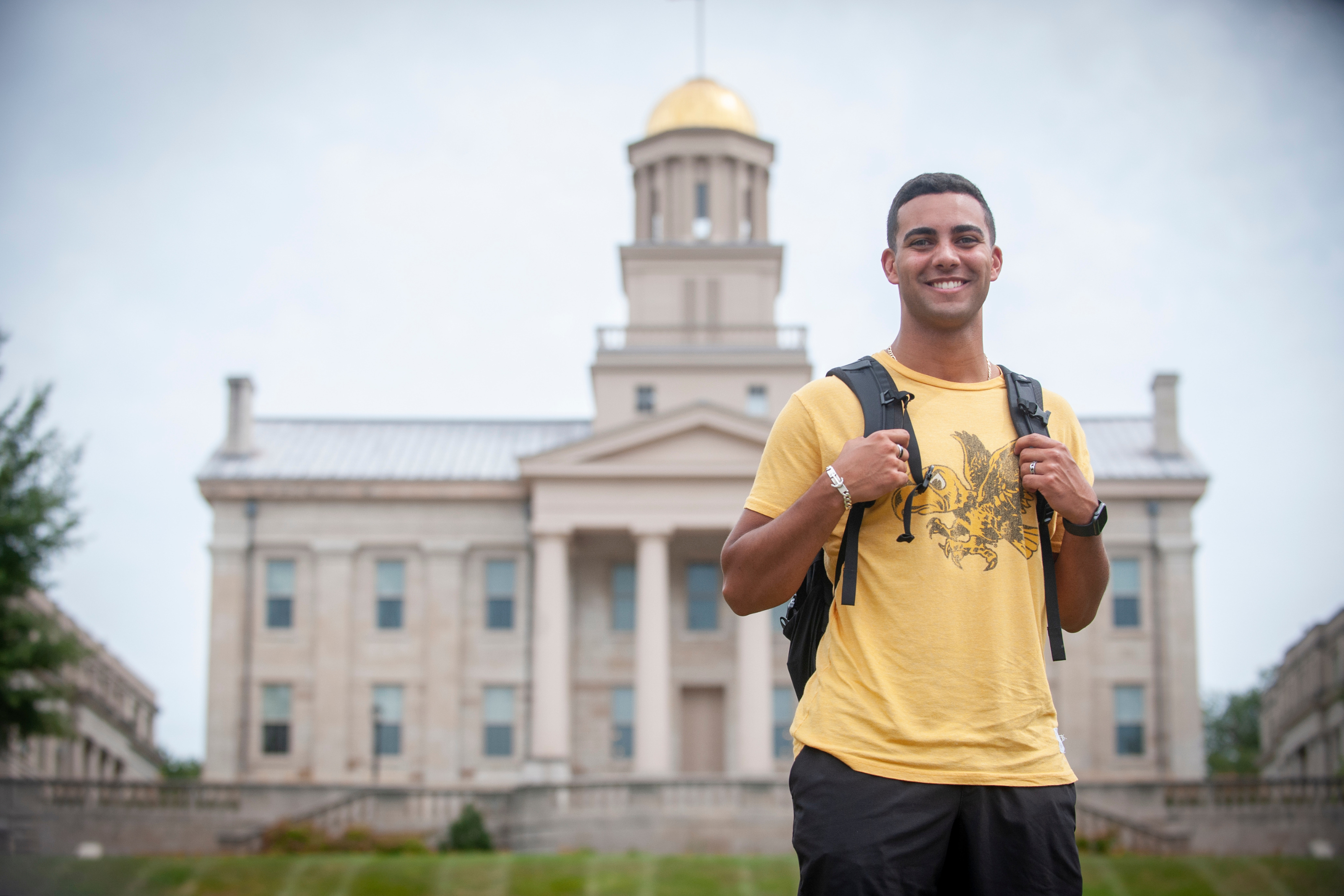 A male student in a Hawk t-shirt stands in the foreground of Old Capitol