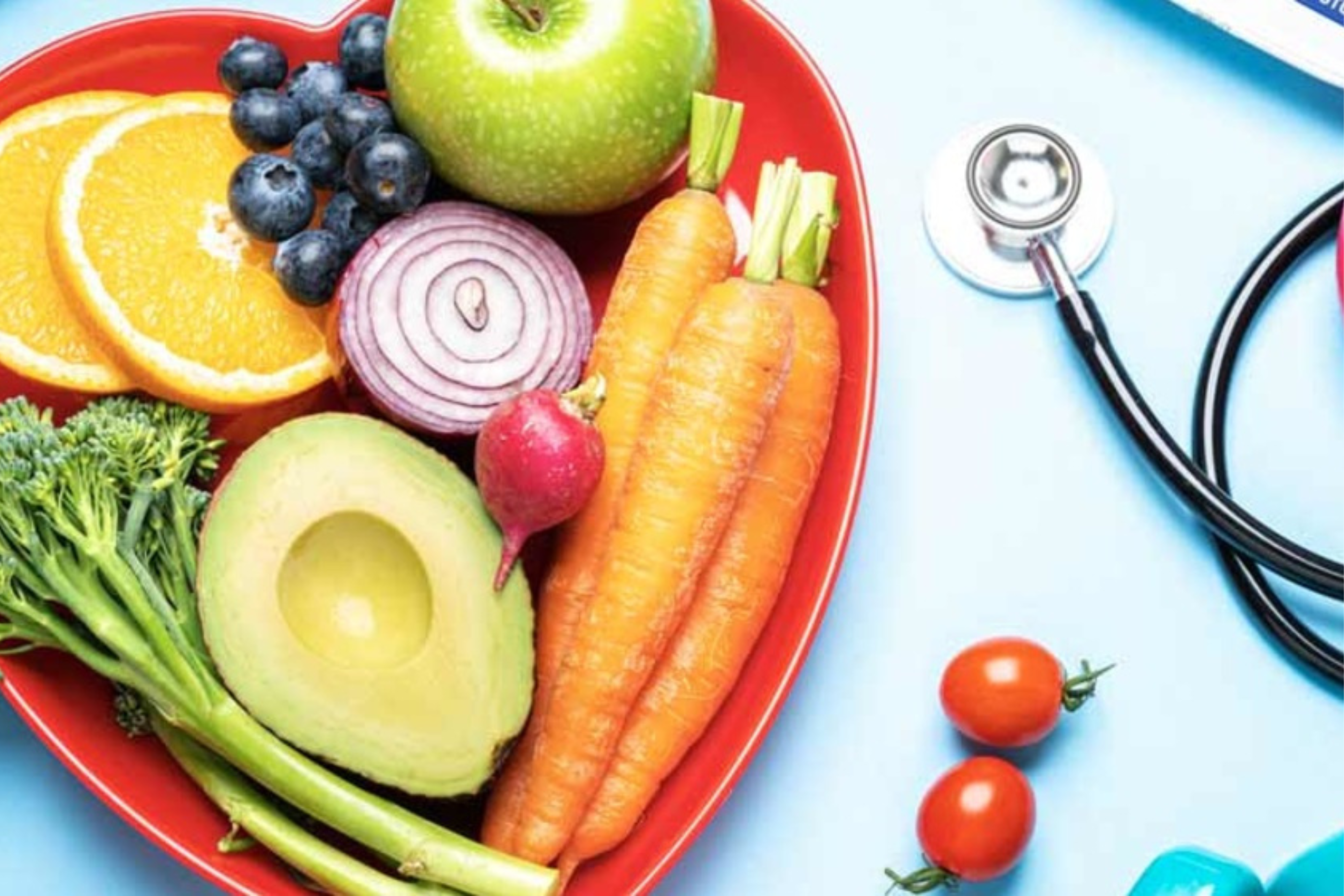A heart-shaped bowl filled with fruit and veggies and a stethoscope on a table