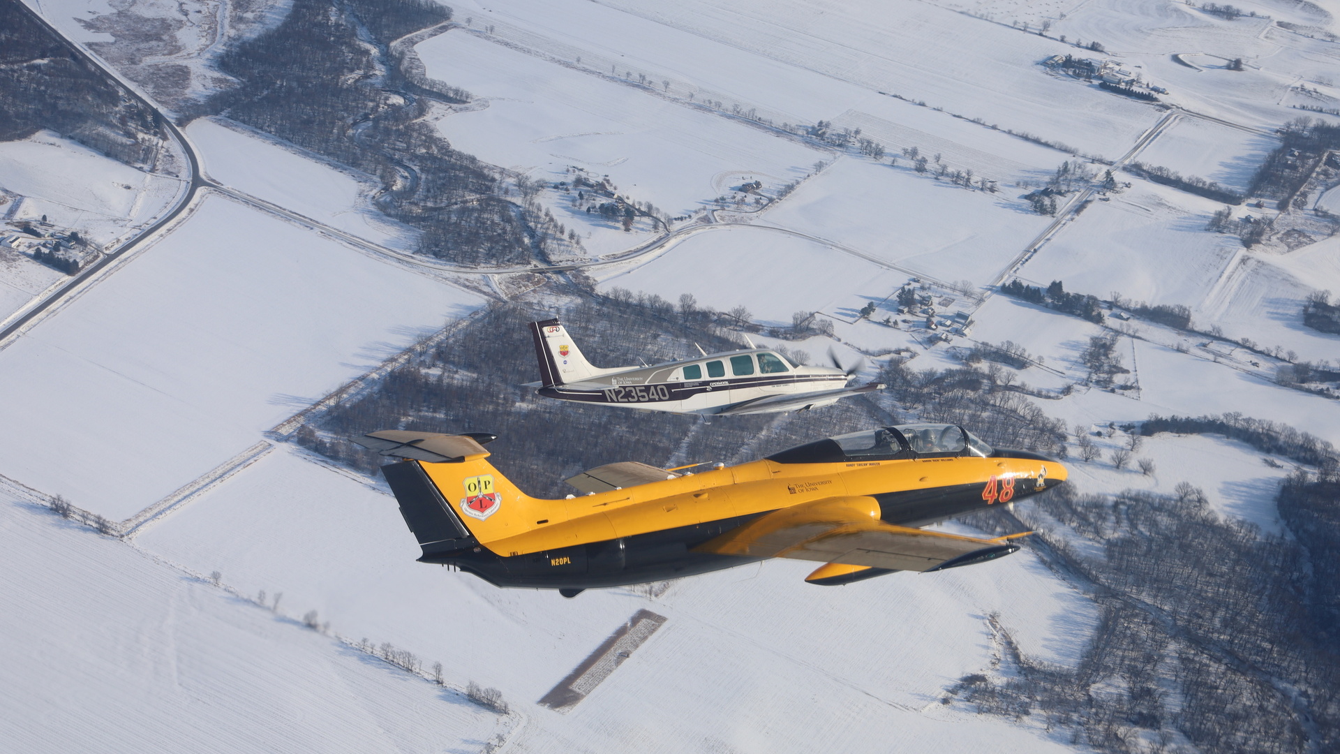 Two aircraft bank in the air with a snowy ground below