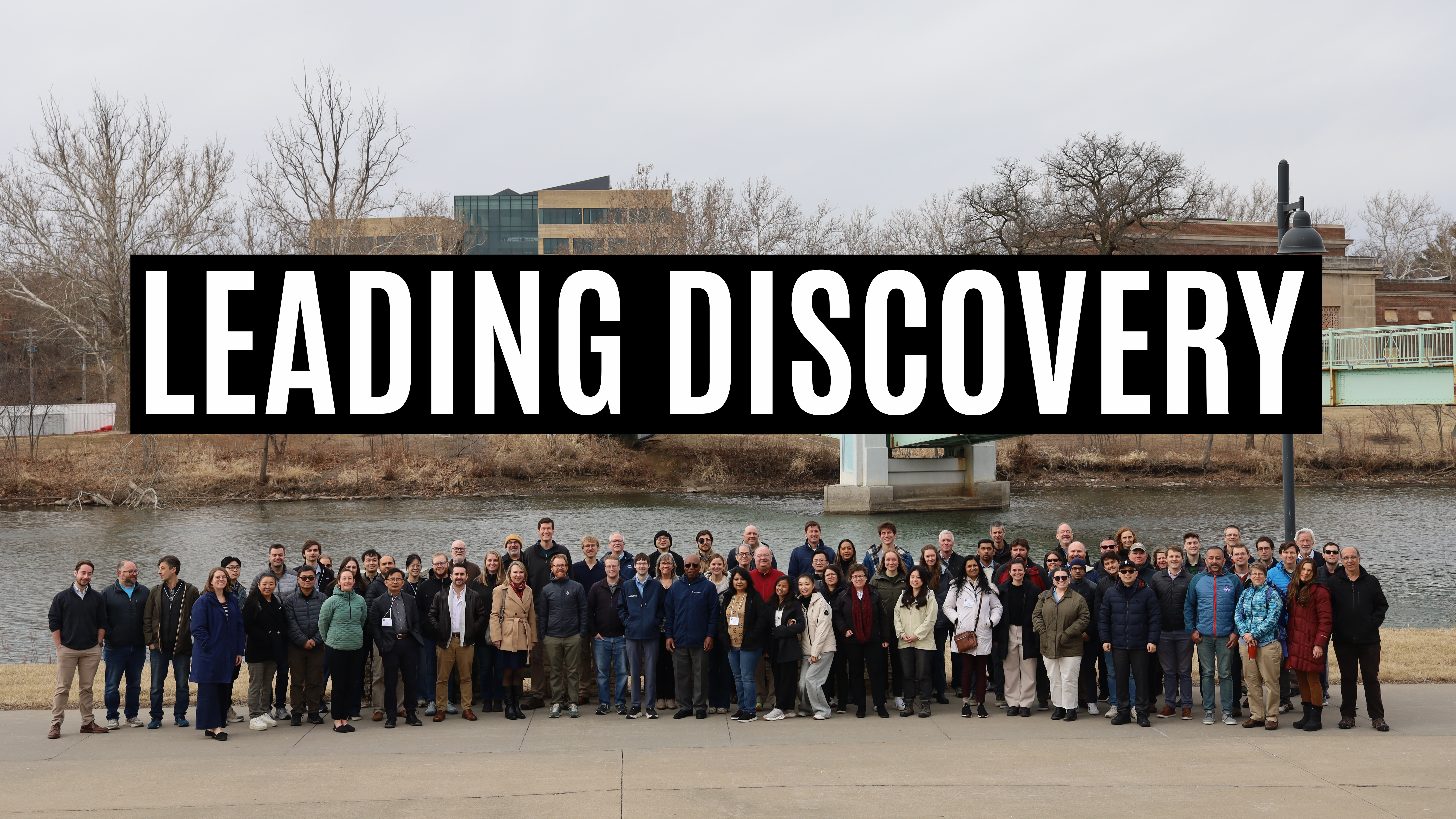 Crowd stands in front of river with light green bridge in the background