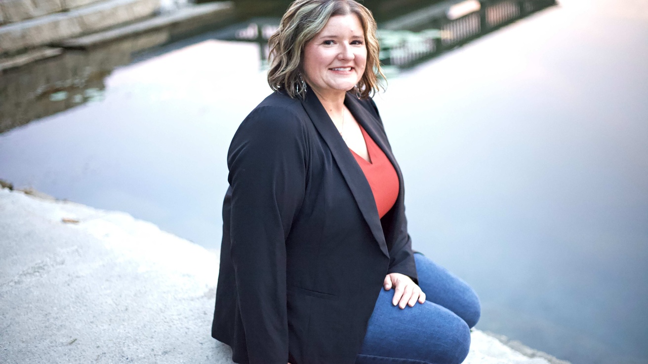 A woman poses in a seated position in front of a body of water