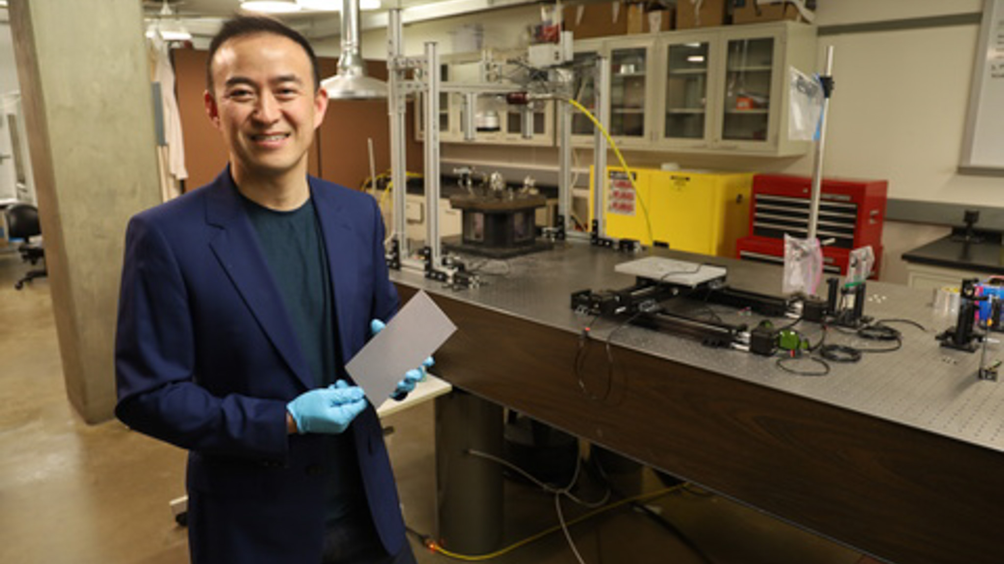 Man poses in laboratory setting holding a piece of metal
