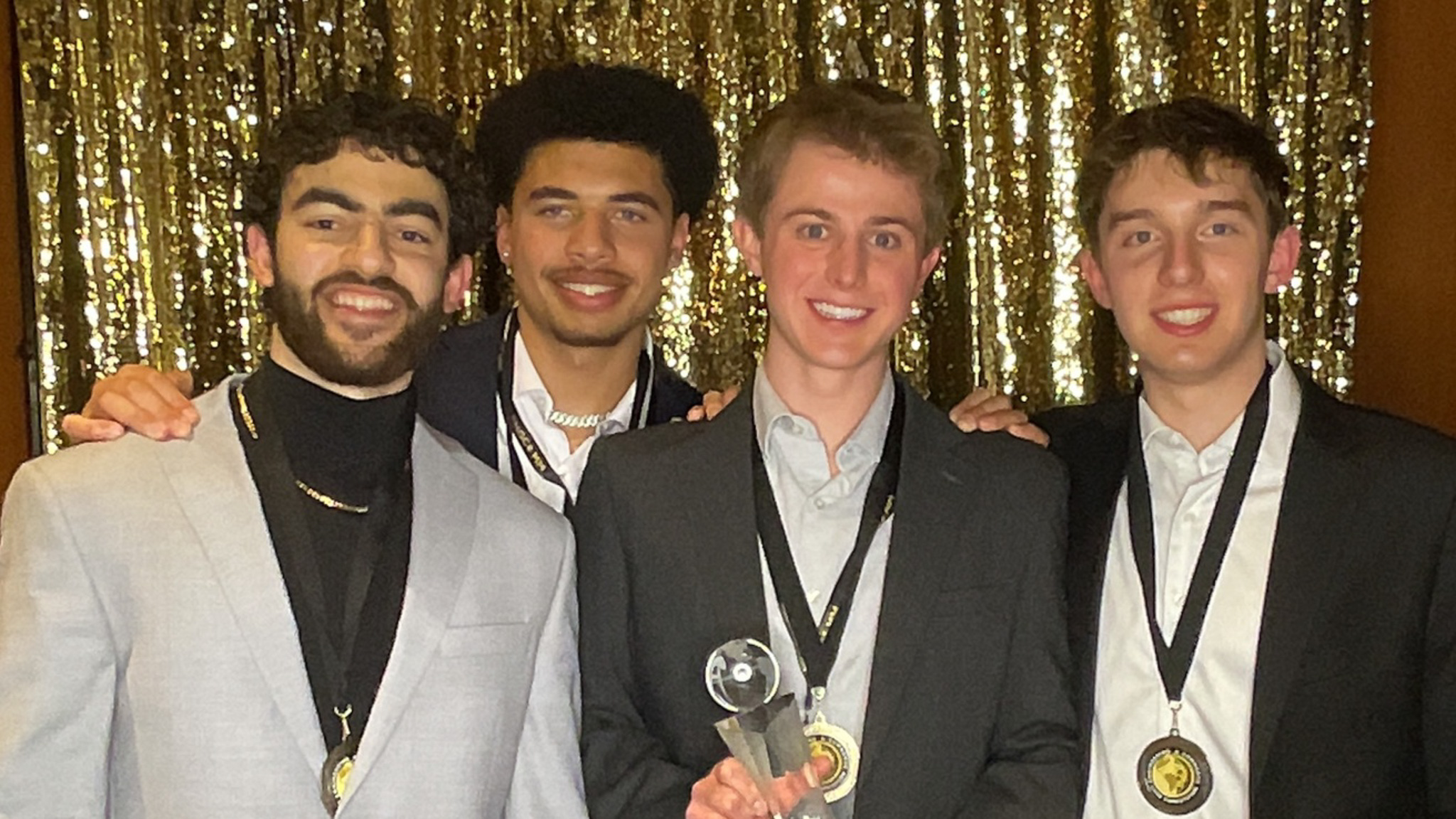 Four young men stand for a picture with the second from left holding a trophy