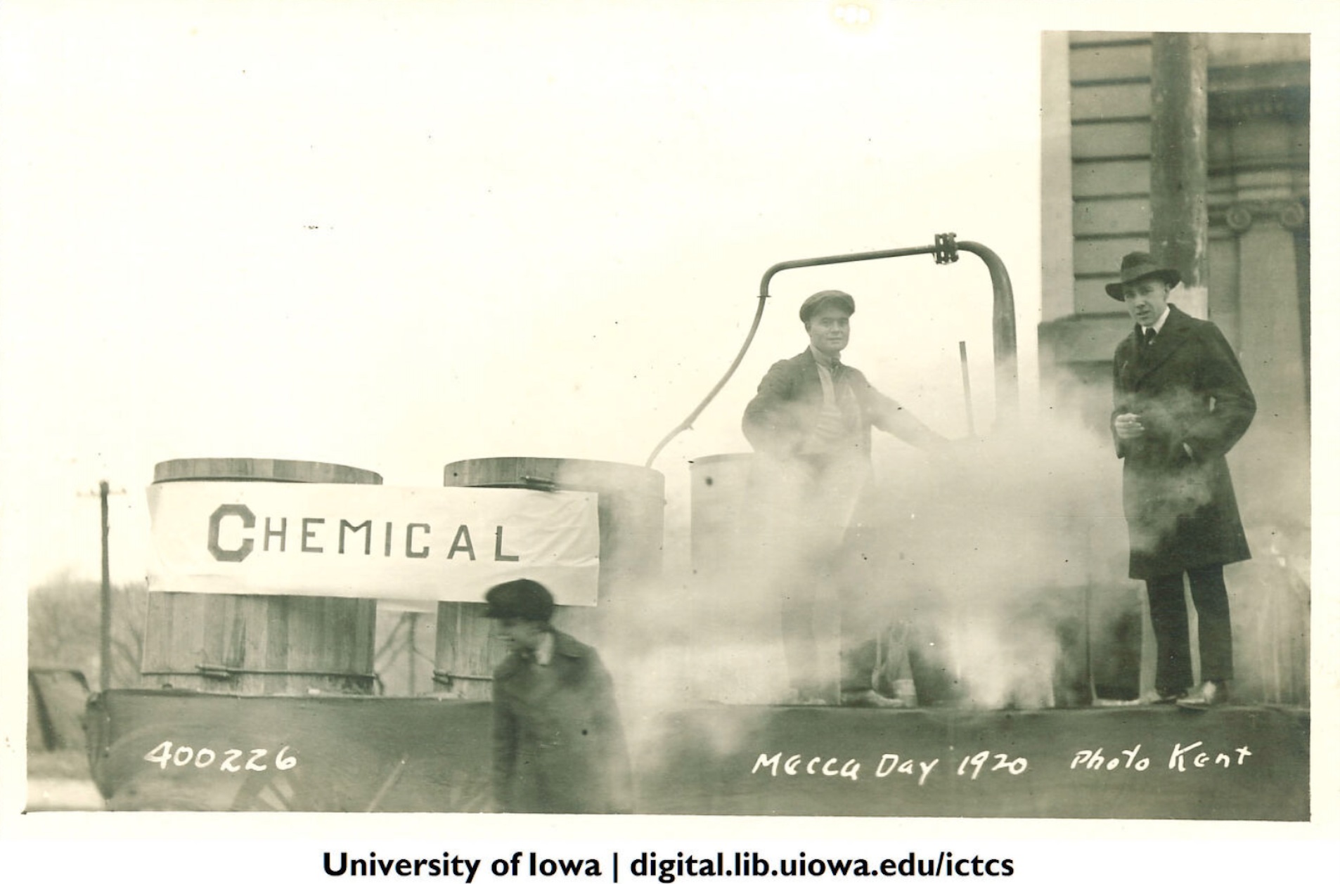Men stand on and in front of a parade float with the word "chemical" inscribed