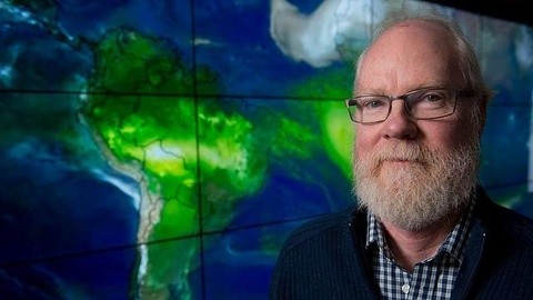 Man with beard and glasses stands in front of map with countries outlined in green.