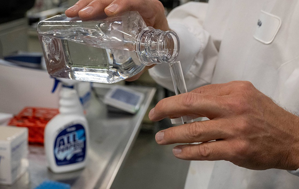 Researcher in a white lab coat pours clean water from a glass container into a test tube