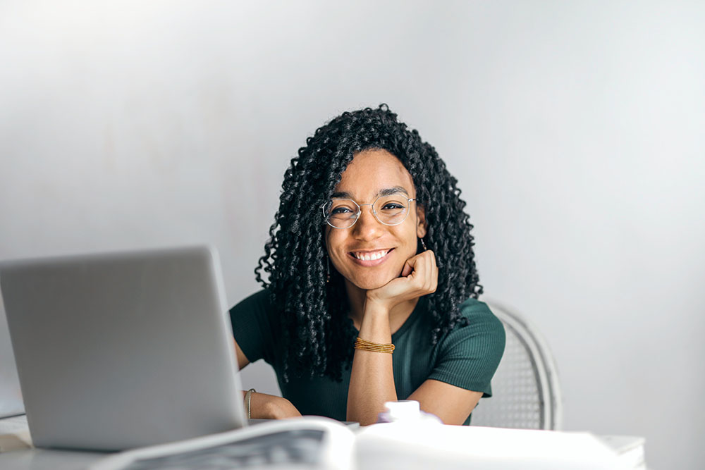 Person sitting at desk in front of a laptop and smiling at the camera. 