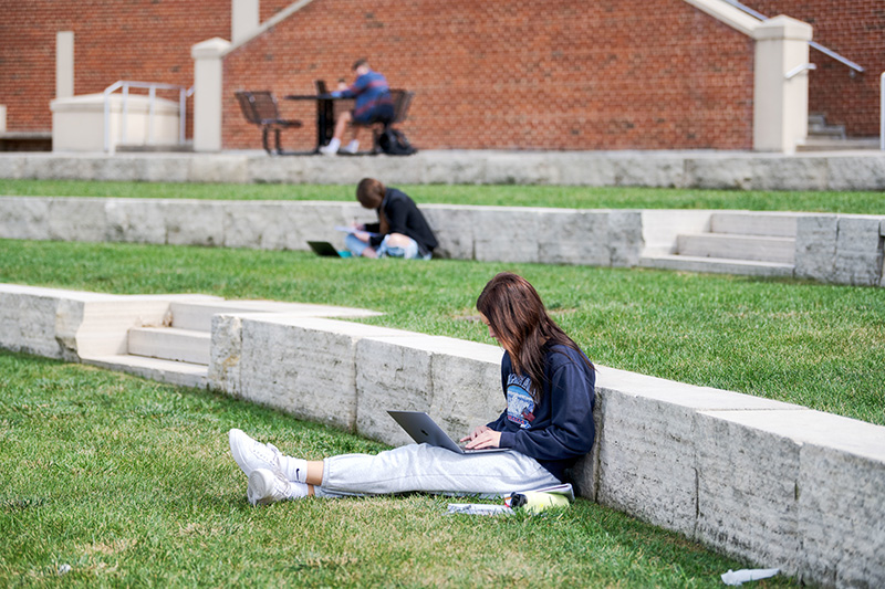 Iowa students sitting in campus greenspace while working on laptops.