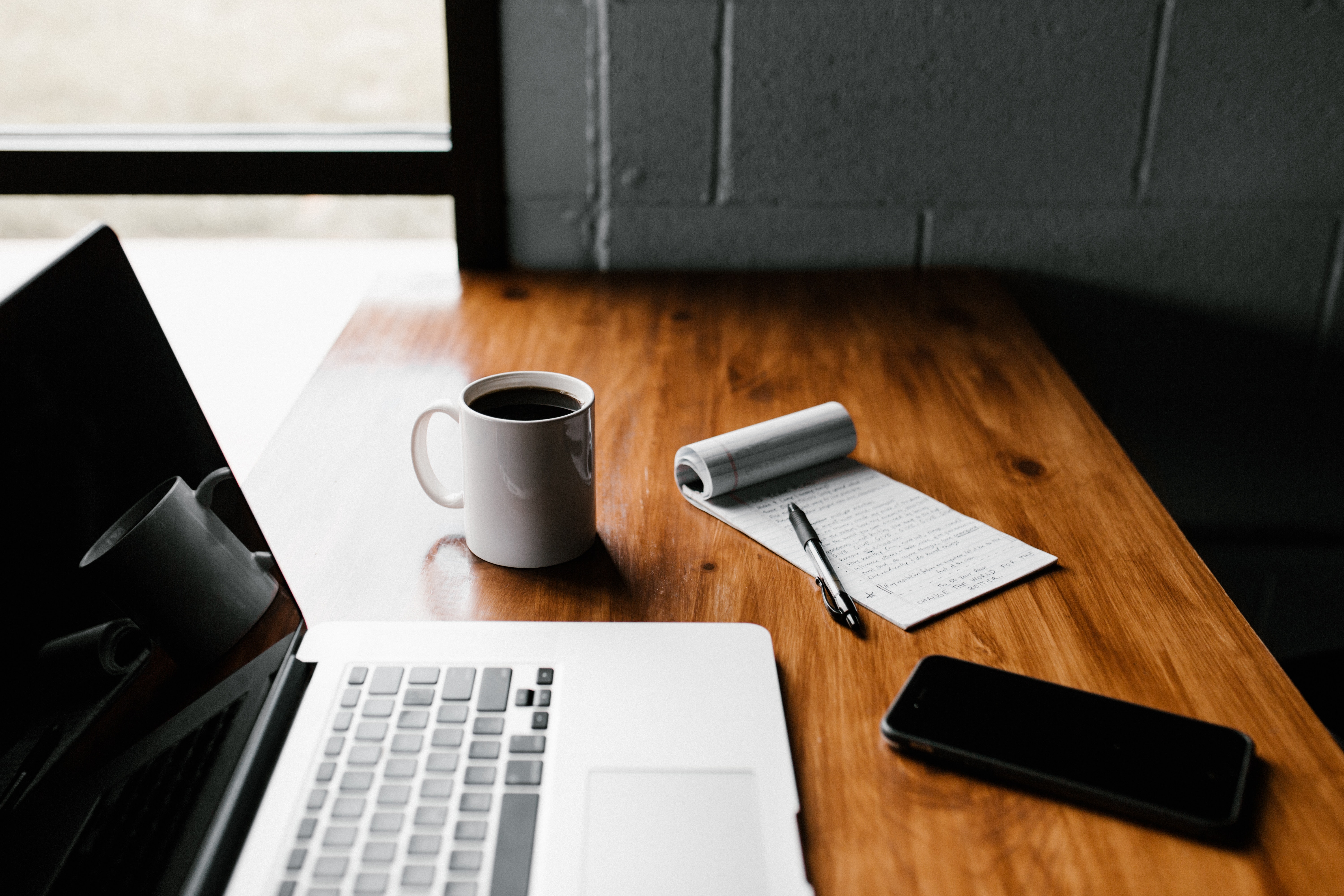 A laptop, coffee cup, and notebook setting on a table. 