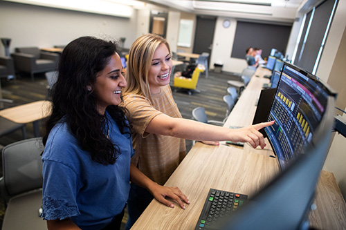 Two UI business students discuss a program on a large monitor.