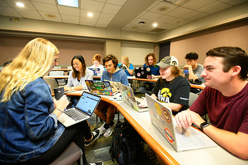 UI students sitting in a group with laptops and collaborating in a marketing course. 