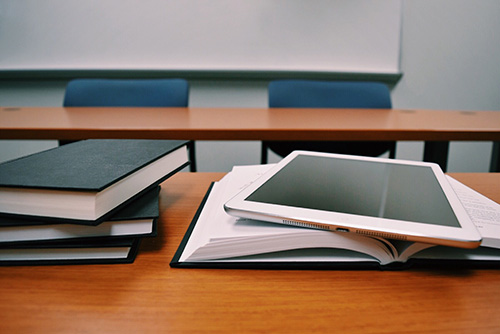 A stack of textbooks on a table with a tablet lying on top of an open book.