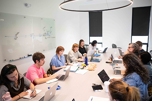 UI students sit around a large table with laptops to participate in a nonfiction writing class.