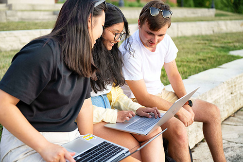 Three UI students sit on the Pentacrest green space with laptops, working together.