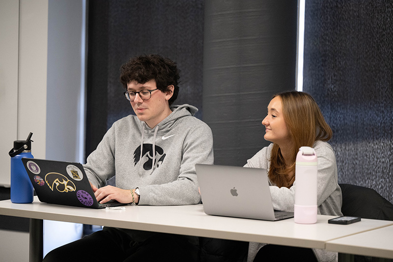 Two students sit at a desk together.