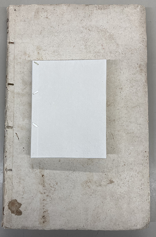 Color image of the discolored white cover of Morgagni's Opuscula miscellanea with a modern white paper cover example book laying on top, 1763.