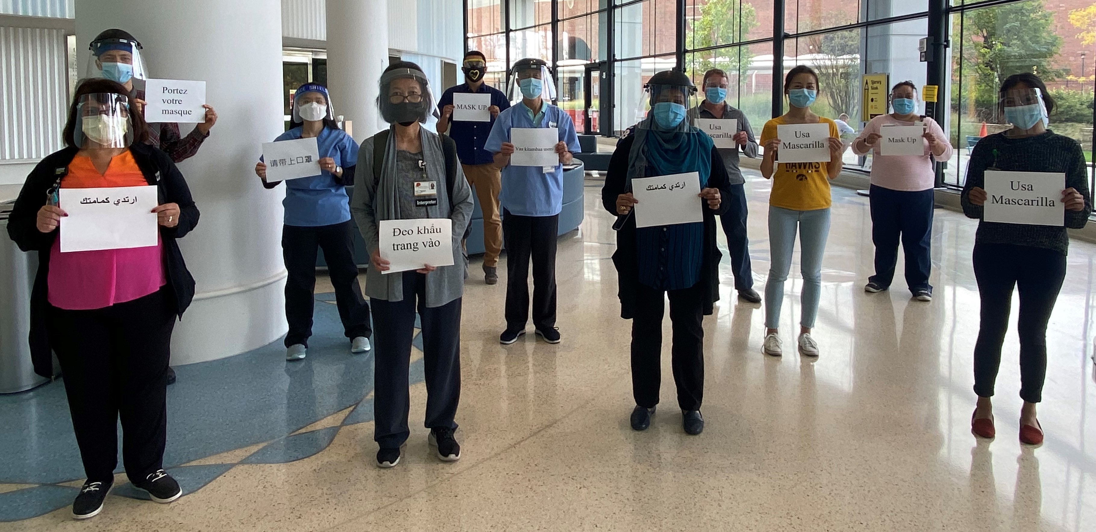 UIHC Interpreters holding signs in Spanish, French, Arabic, Swahili, Vietnamese and Mandarin that state “mask up” or “wear your mask”.