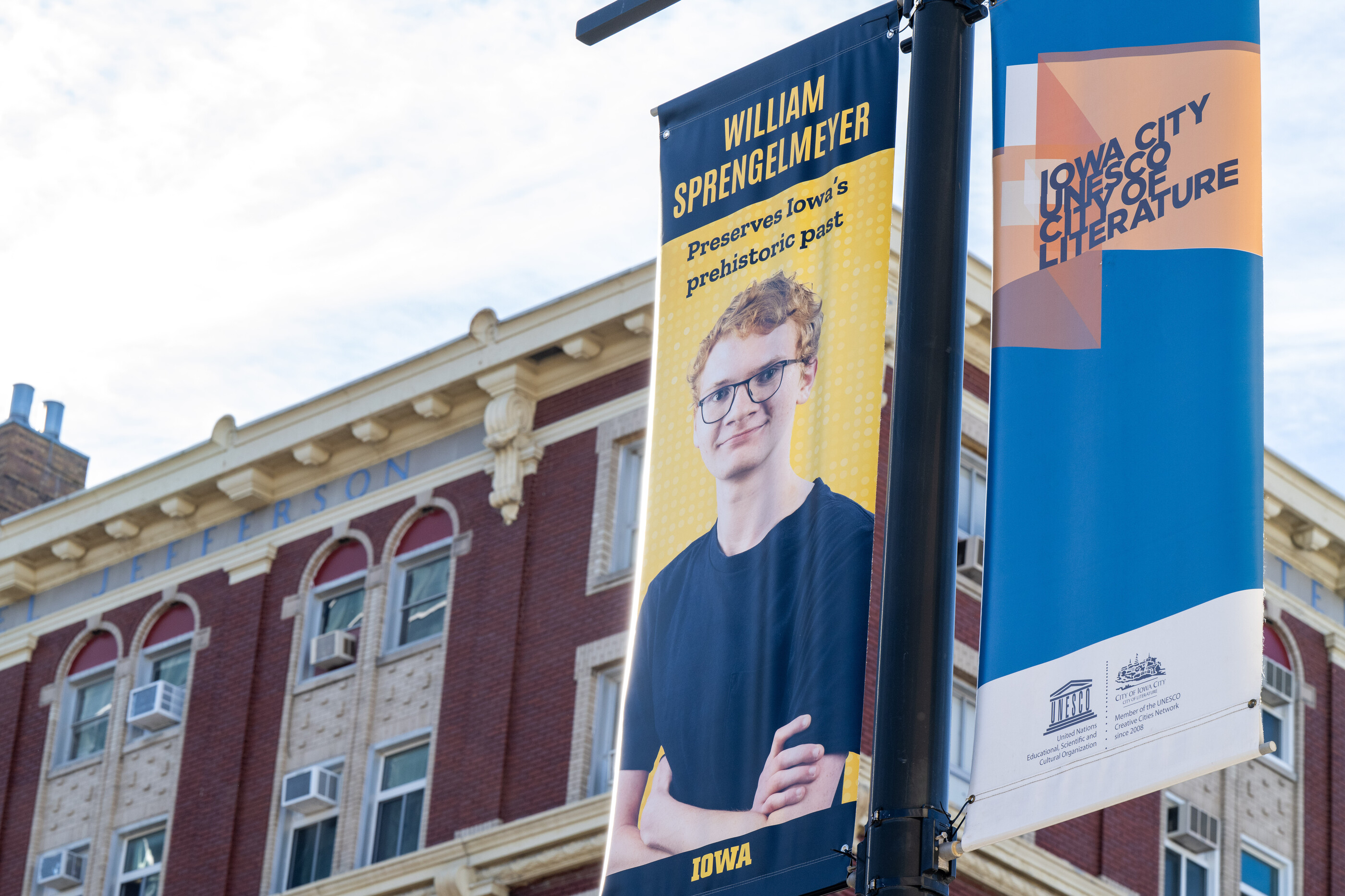 A banner of undergraduate researcher William Sprengelmeyer hangs in front of the Hotel Jefferson in Iowa City