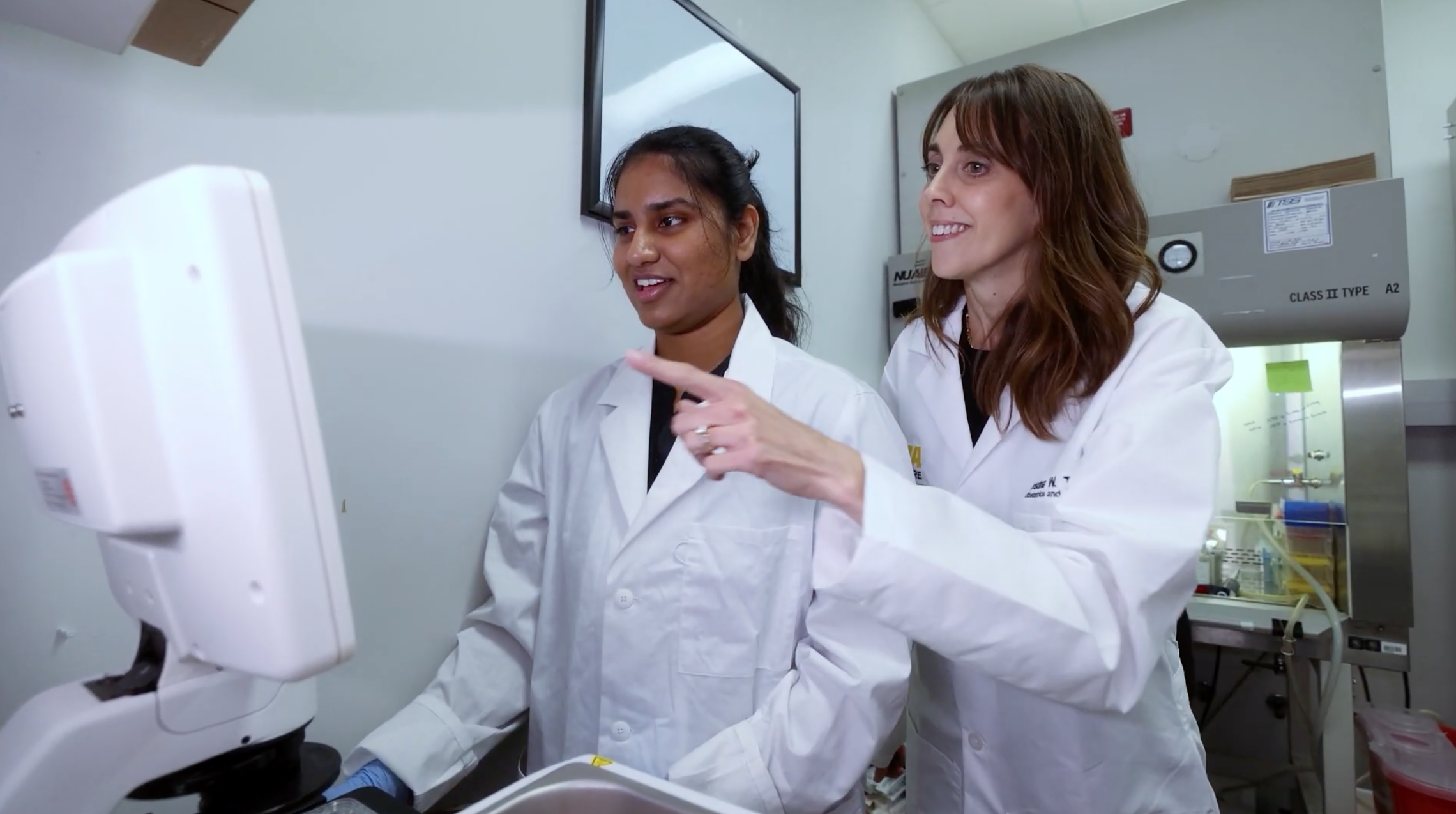 Hiruni Sumanasiri and researcher look at the screen of a microscope