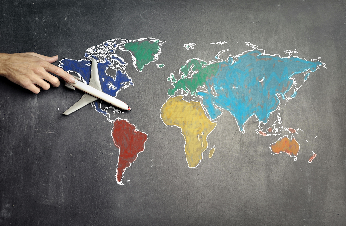 Someone pushing a toy airplane over a world map drawn on chalkboard