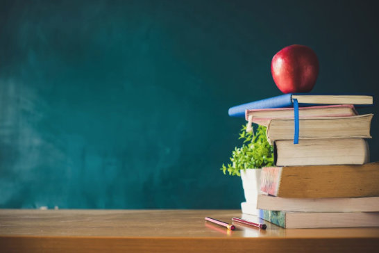 Stack of books and an apple in front of a chalkboard 