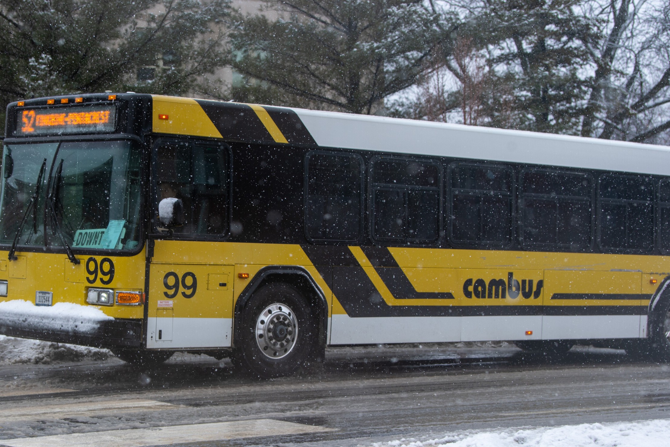 Light snow falling around a yellow, black, and white Cambus bus.
