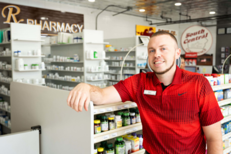 Mylo Wells, wearing a red polo shirt and  leaning on a shelf in a pharmacy