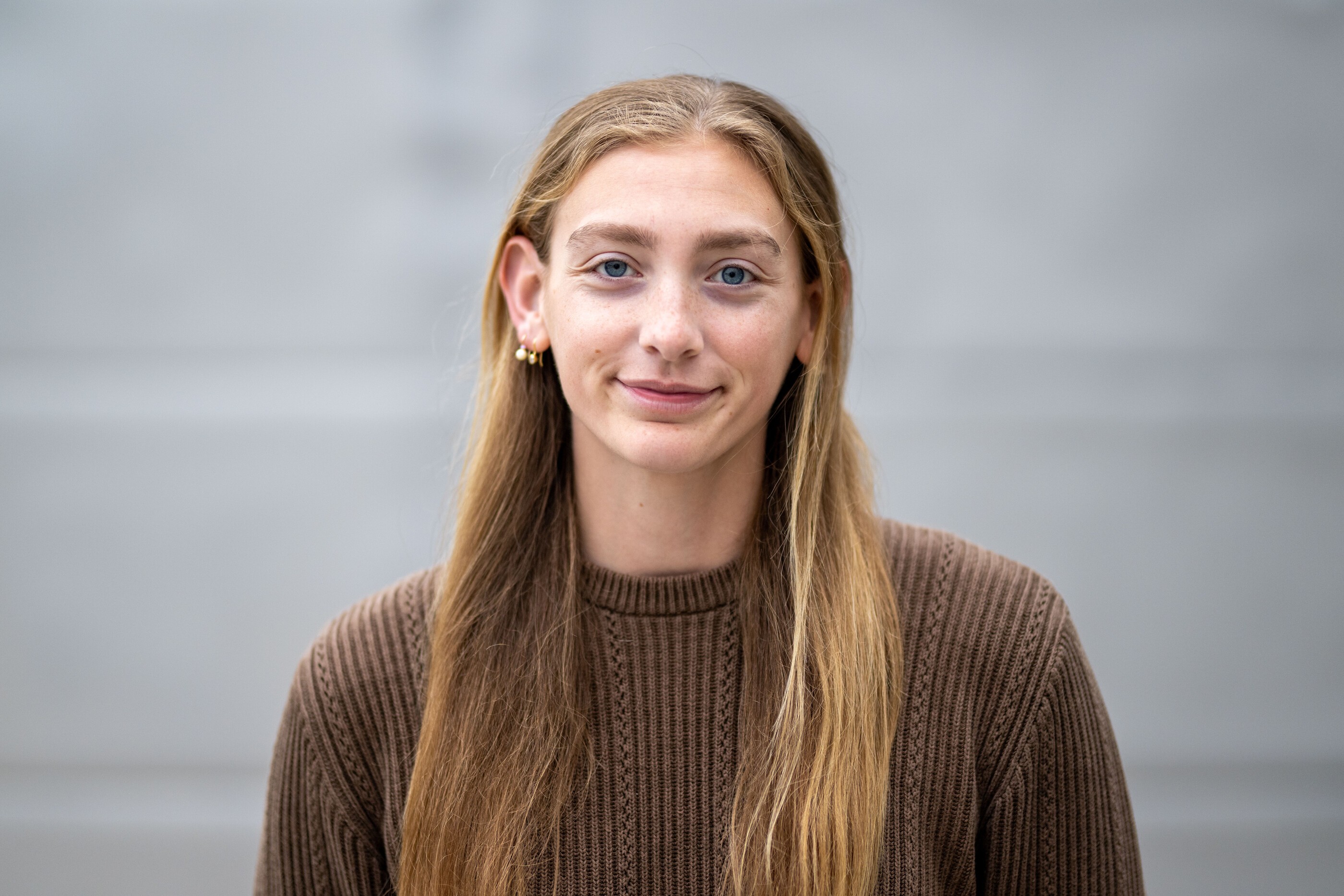 Nina Osborne, an undergraduate student, with long, dark blond hair, slightly smiling, and wearing a brown sweater. 