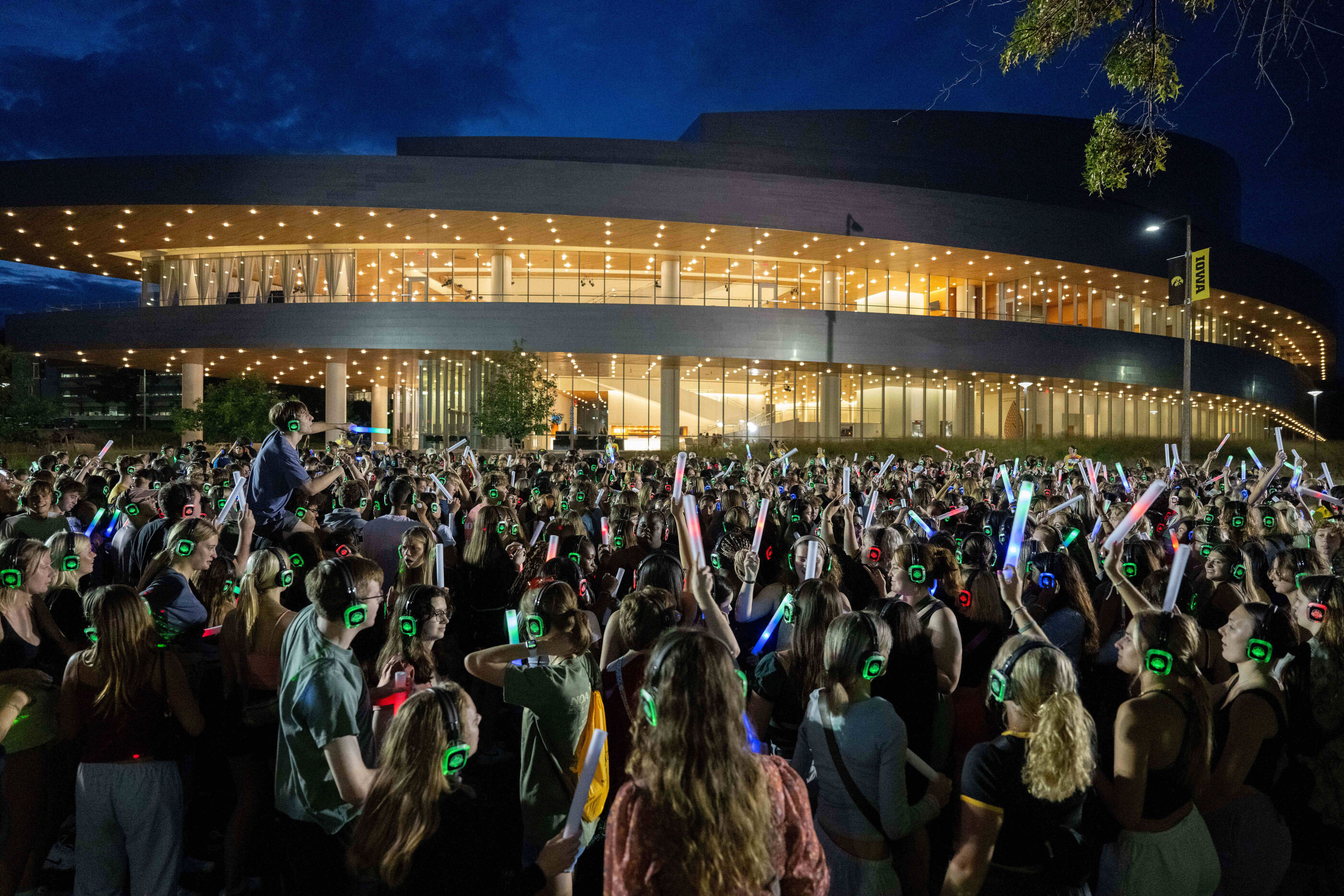 A crowd of people with glow lights and wearing headphones outside Hancher Auditorium