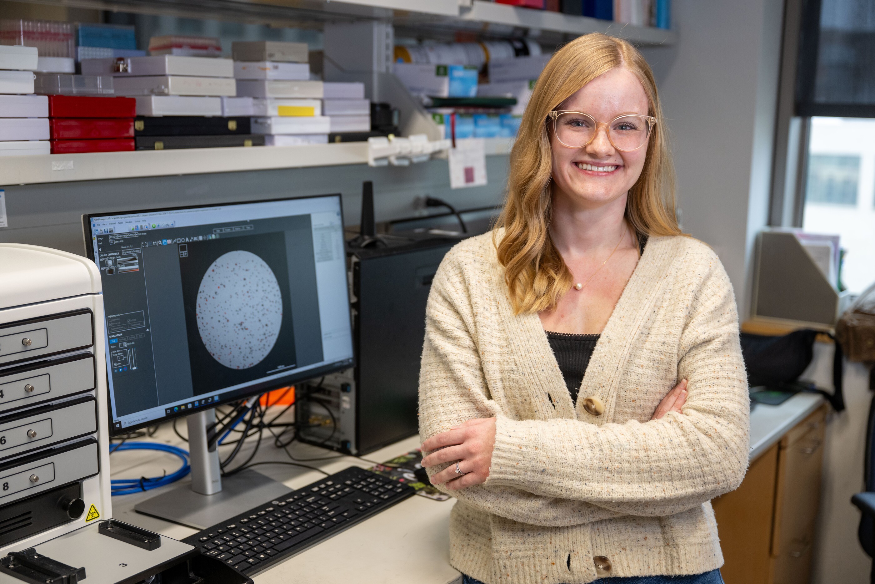 Katie Colling stands in her laboratory in front of a monitor displaying a tumor cell.