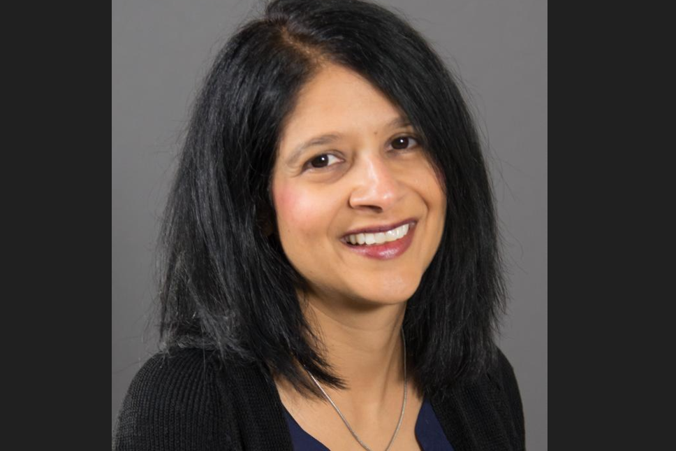Saba Rasheed Ali, a smiling woman with mid-length black hair, wearing a black cardigan and blue shirt. 
