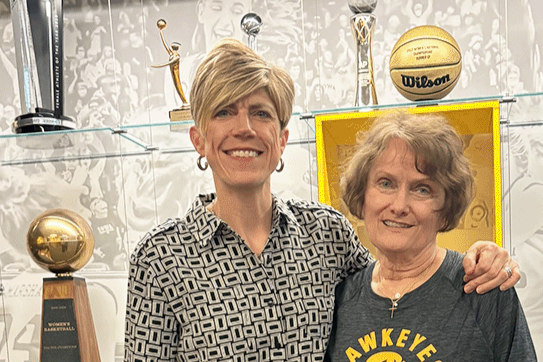 Iowa Women's Basketball coach Jan Jensen and UI alum Sheryl Stoll standing in front of a case of basketball trophies.