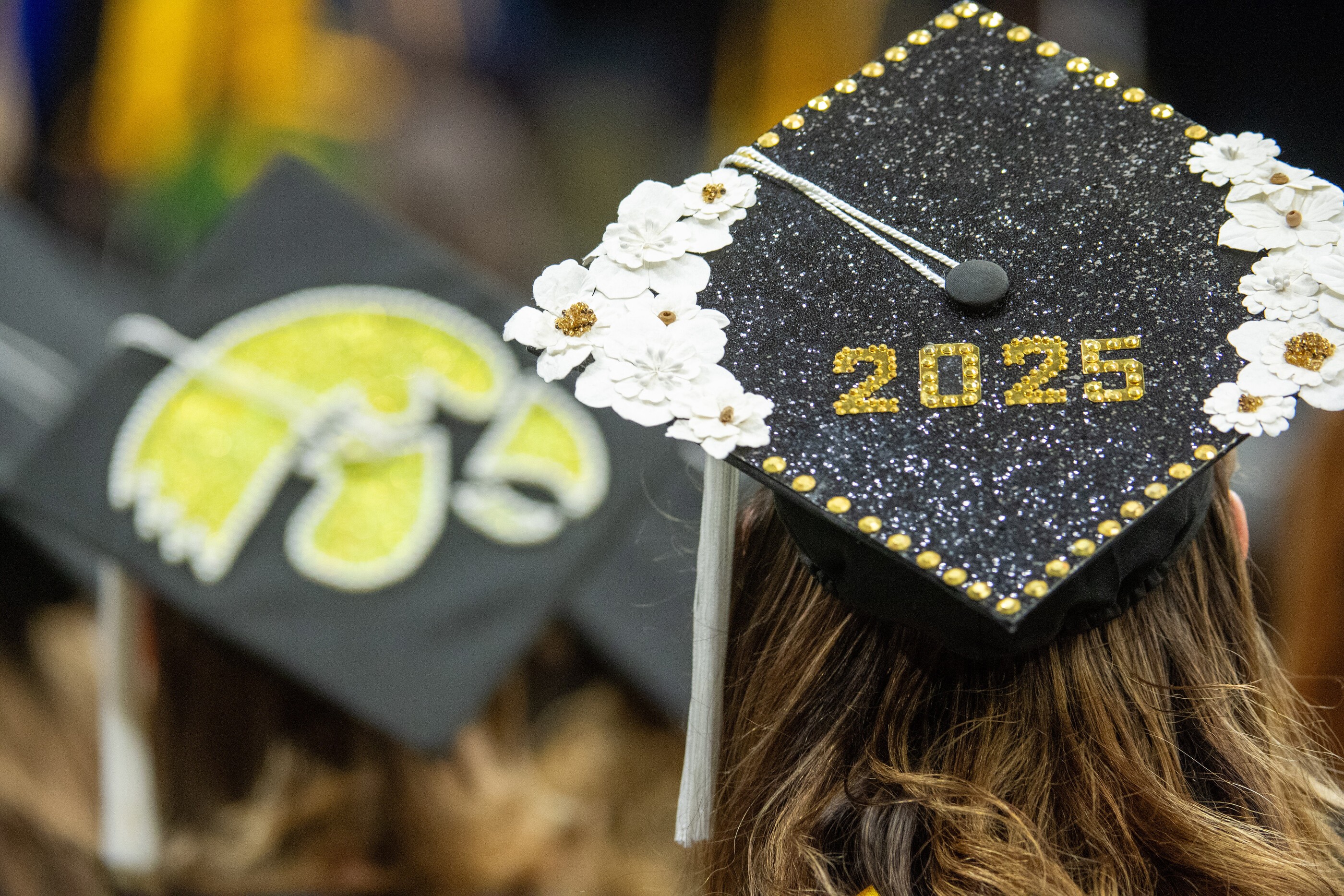 A close-up of a graduation cap adorned with glitter, sequins and flowers.