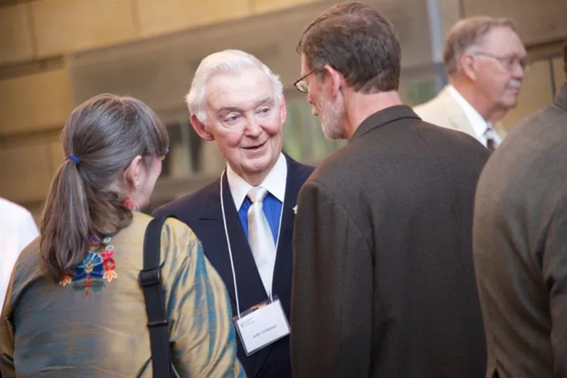A picture of John Colloton speaking with a group of people.