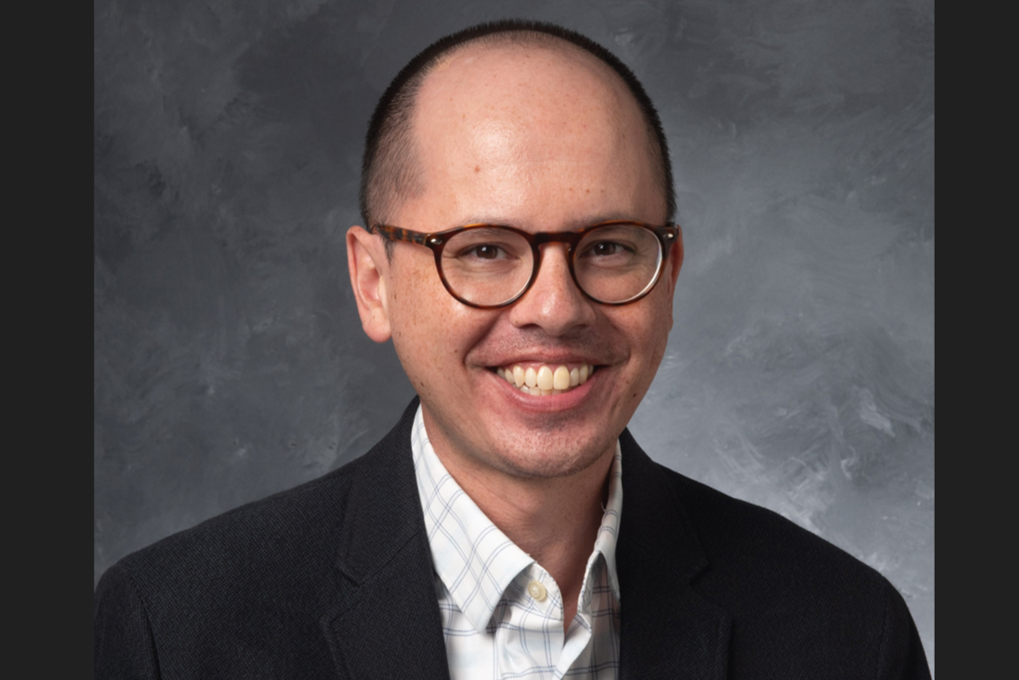 Shawn Datchuk, a UI professor with short black hair and a big smile, wearing glasses and a dark suit