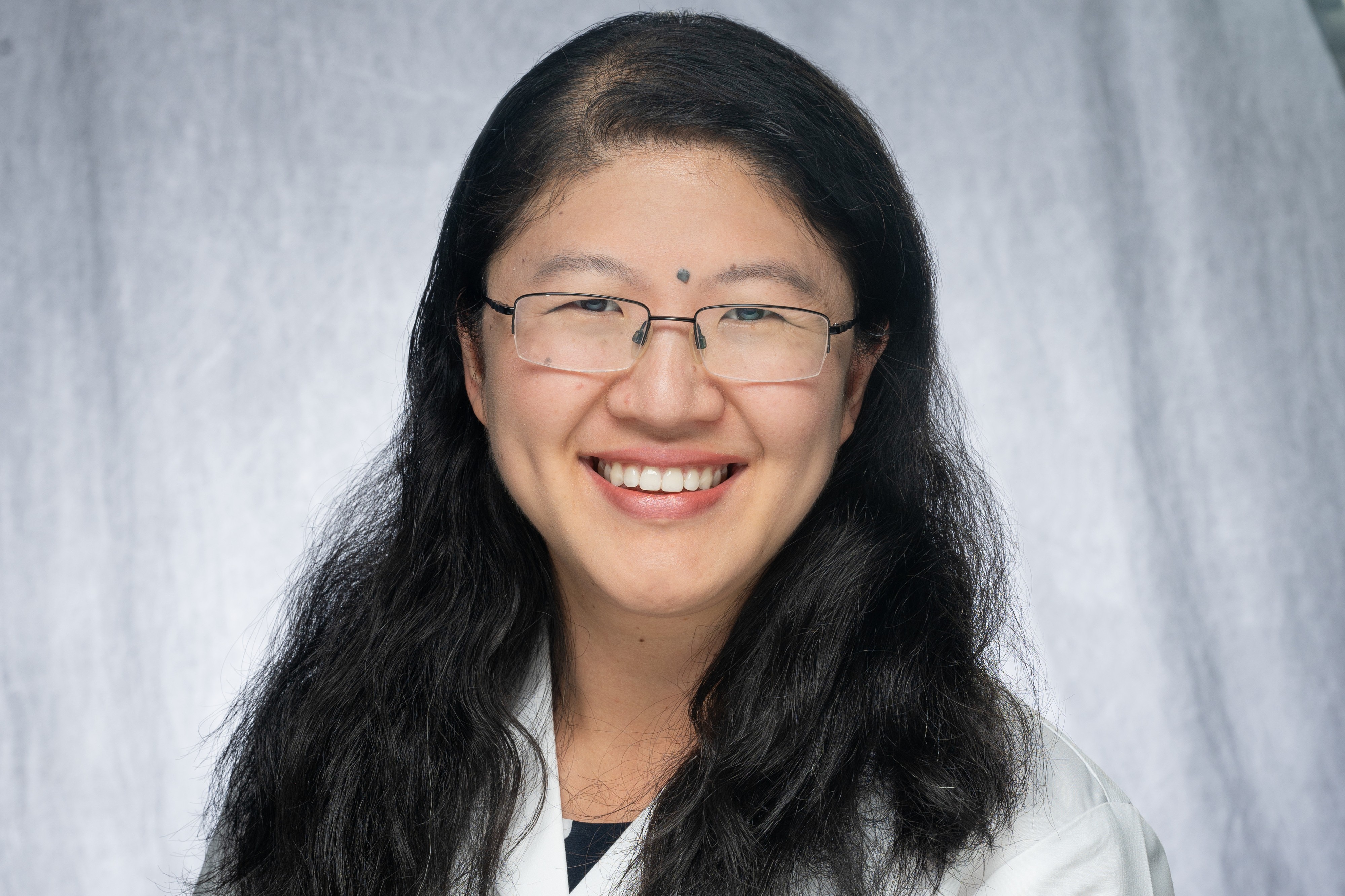 Susan Shen, with long black hair wearing glasses and white coat.