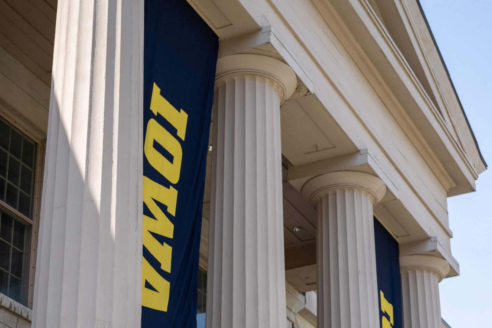 A close-up of the columns of the Old Capitol museum, with black banners that says IOWA hanging between the columns.
