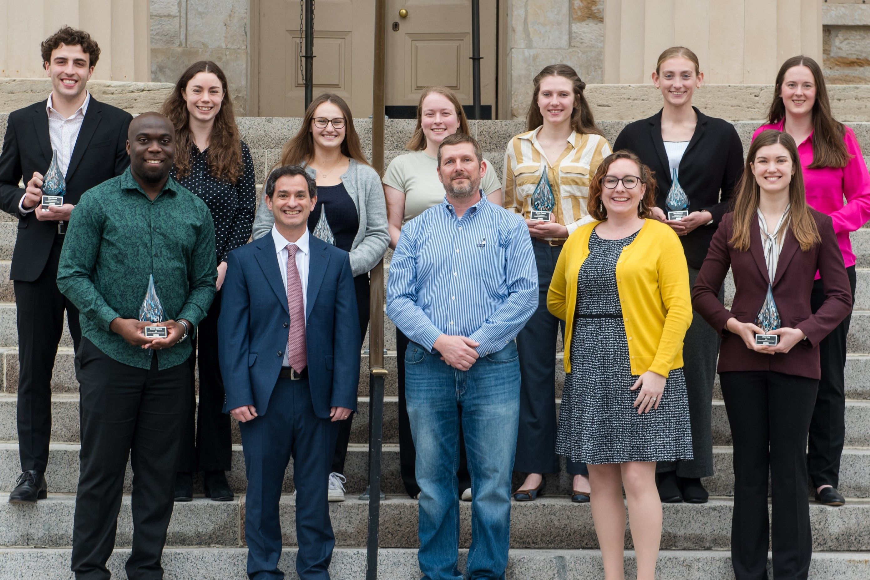 The twelve winners of the OVPR  awards, standing in two rows outside on the steps of a building
